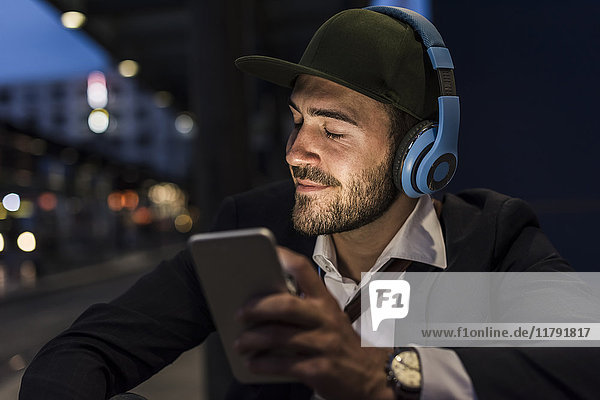 Junger Mann in der Stadt mit Kopfhörer und Handy am Abend