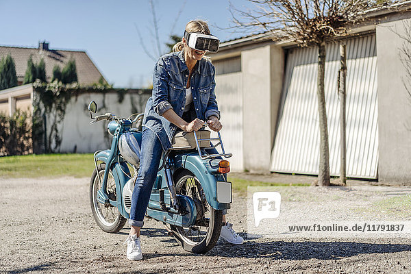 Frau sitzend rückwärts auf Oldtimer-Motorrad mit VR-Brille