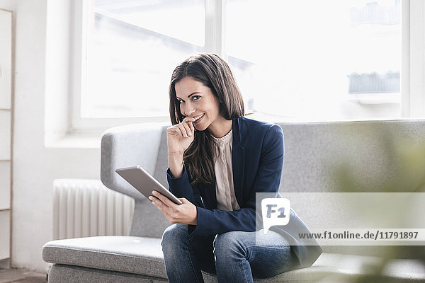 Portrait of smiling businesswoman with tablet on couch