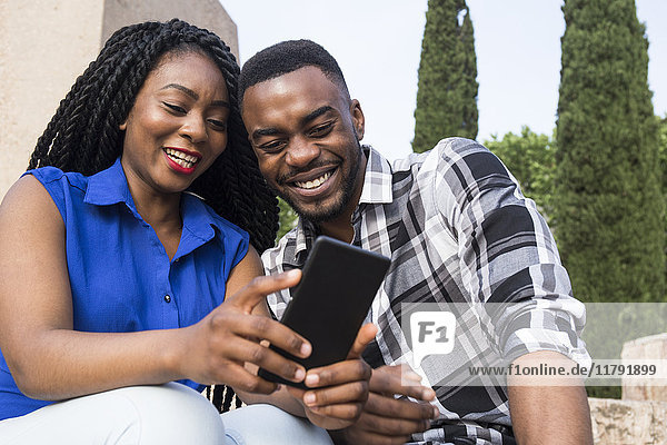 Porträt eines lächelnden jungen Paares beim Blick aufs Handy