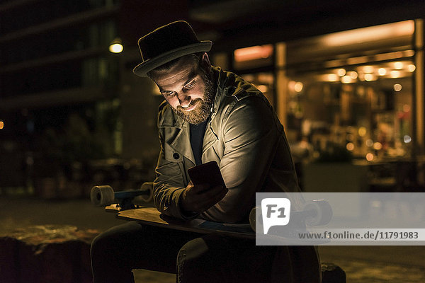 Stilvoller junger Mann mit Handy in der Stadt bei Nacht