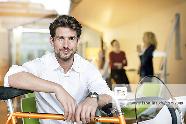 Ein junger Geschäftsmann im Büro  der sich auf sein Rennrad stützt.