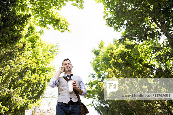 Geschäftsmann mit Kaffee und Smartphone im Stadtpark