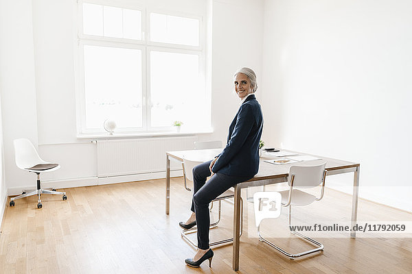 Lächelnde Geschäftsfrau im Büro auf dem Tisch sitzend