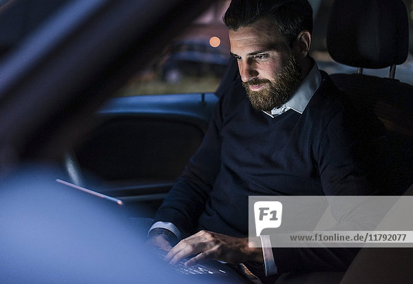 Businessman using laptop in car at night