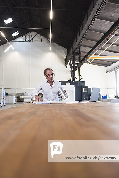 Mann mit Plan  Produkt und Laptop auf dem Tisch in der Fabrik