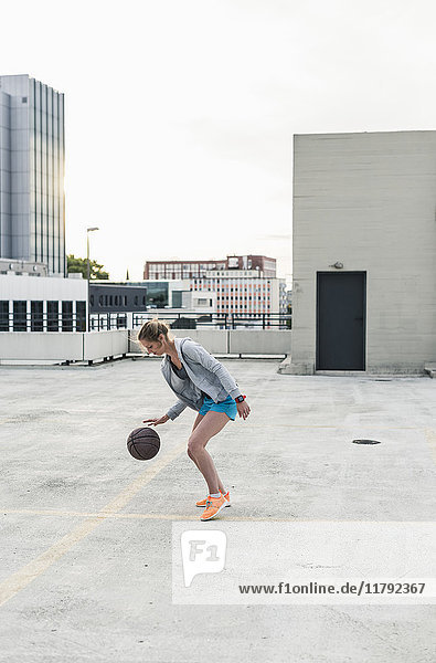Frau spielt Basketball auf Parkdeck in der Stadt