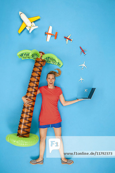 Woman holding inflatable palm tree and laptop with airplanes coming out