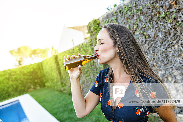Junge Frau beim Biertrinken am Pool
