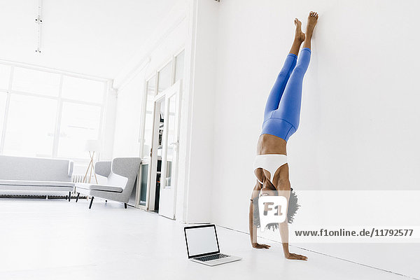 Young woman practising yoga with laptop by her side