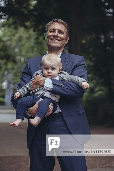Portrait of smiling mature businessman holding baby boy outdoors