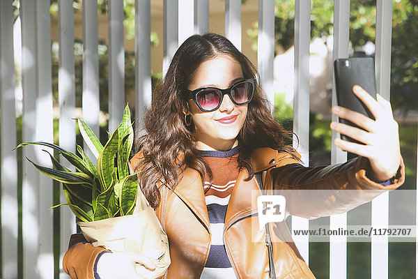 Junge Frau mit Topfpflanze  die Selfie mit Smartphone nimmt