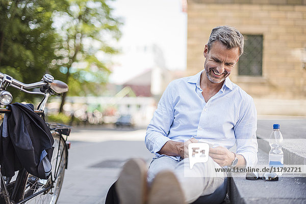 Lächelnder Mann sitzt auf der Treppe in der Stadt mit dem Handy