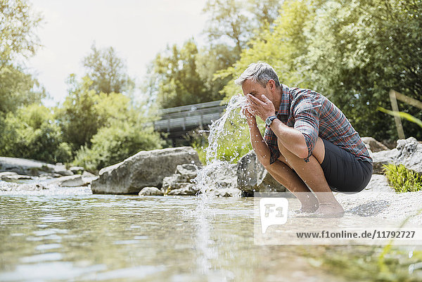 Wanderer macht eine Pause am Flussufer und wäscht sich das Gesicht.