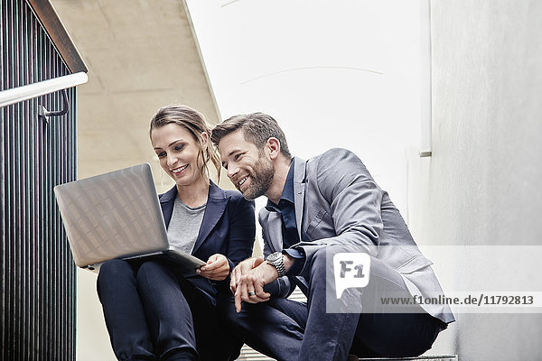 Businessman and businesswoman sitting on stairs in office sharing laptop