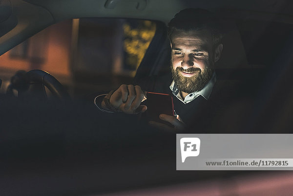 Smiling businessman using cell phone in car at night