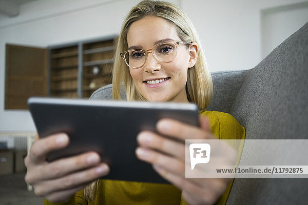 Porträt einer lächelnden Frau mit Brille auf der Couch mit Mini-Tablette