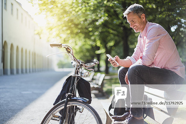 Lächelnder Mann mit Fahrrad beim Telefonieren auf einer Parkbank