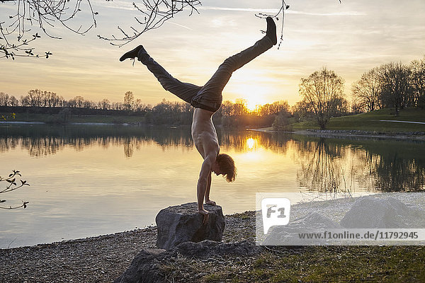 Germany  Bavaria  Feldkirchen  man doing a handstand at lakeshore