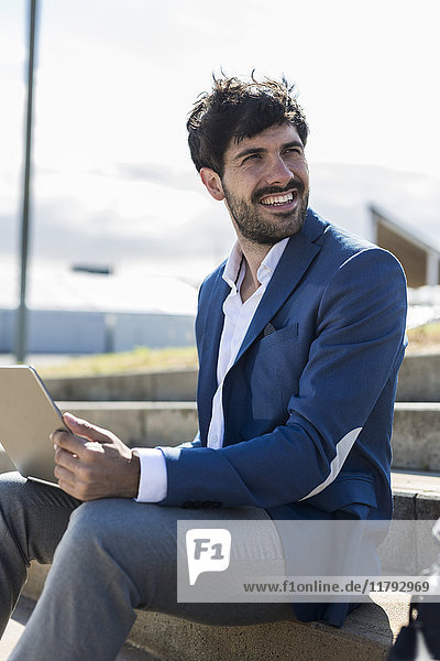 Smiling young businessman sitting on stairs with laptop turning round
