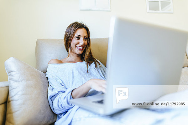Porträt eines lächelnden Jungen auf der Couch mit Laptop