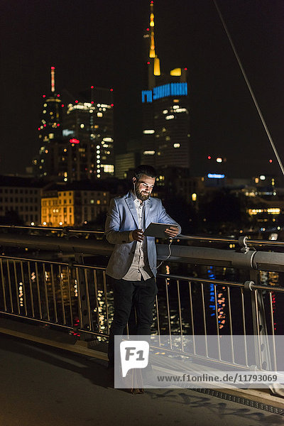 Young man with tablet and earphone on urban bridge at night