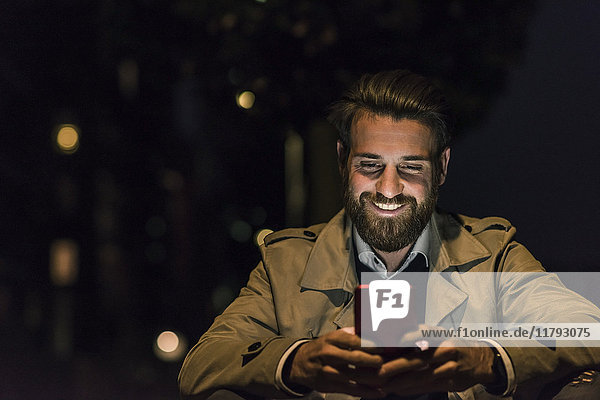 Smiling young man with cell phone in the city at night