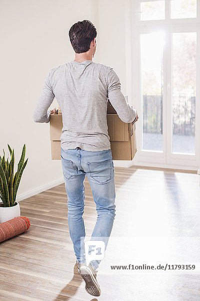 Young man carrying cardboard box in new home