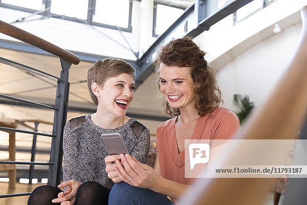 Zwei glückliche Frauen im modernen Büro teilen sich das Handy