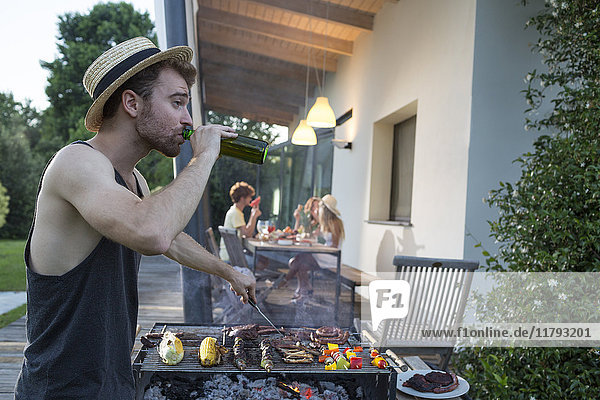 Man having a beer at barbecue grill with friends in background