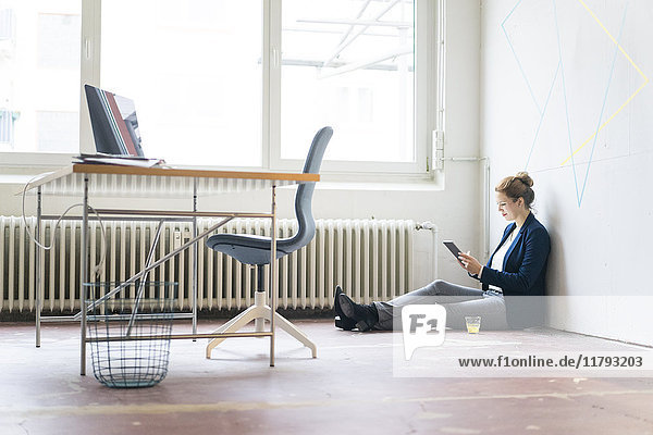 Geschäftsfrau im Büro auf dem Boden sitzend mit digitalem Tablett