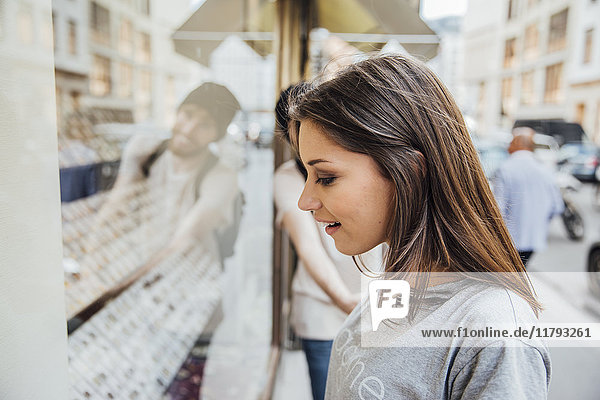 Young woman looking fascinated in shop window  boyfriend trying to pull her away