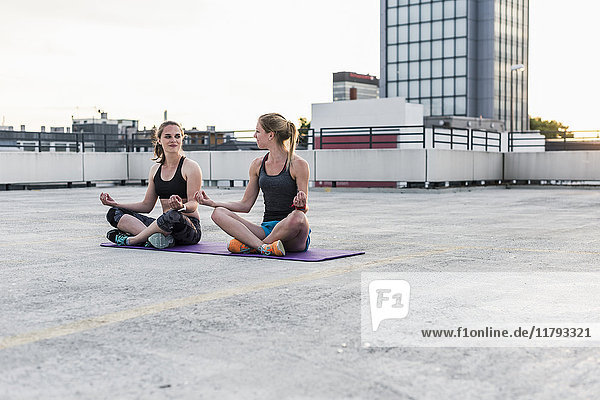 Two women practicing yoga on parking level in the city