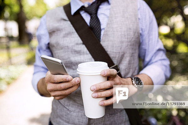 Nahaufnahme eines Geschäftsmannes mit Kaffee und Smartphone im Stadtpark