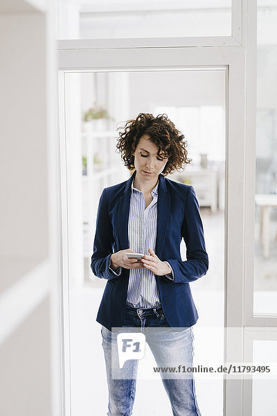 Geschäftsfrau in der Bürotür stehend  mit Smartphone
