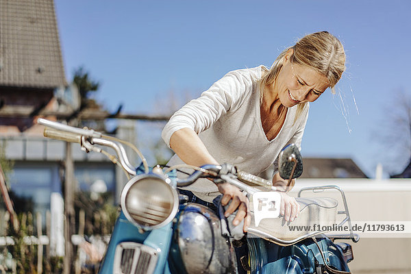Smiling woman cleaning vintage motorcycle