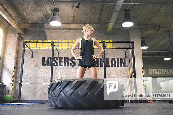 Young woman exercising with tractor tyre in gym