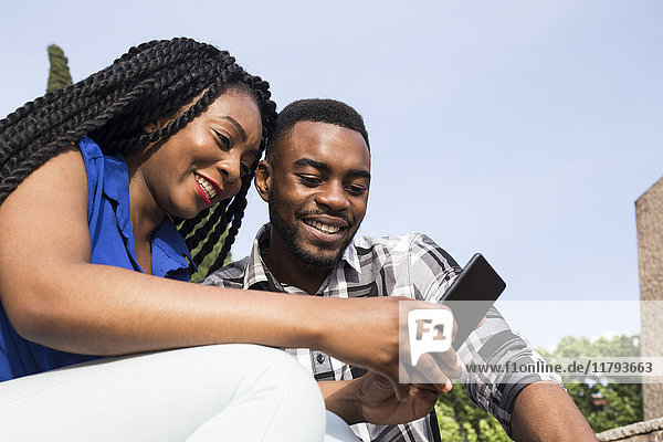 Porträt eines lächelnden jungen Paares beim Blick aufs Handy