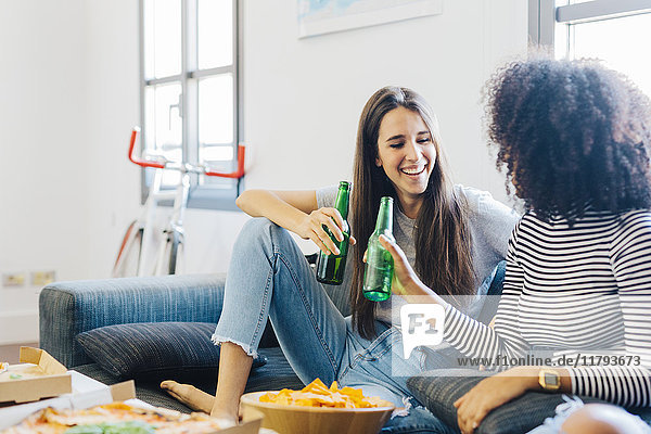 Freunde klirrende Bierflaschen auf dem Sofa sitzend