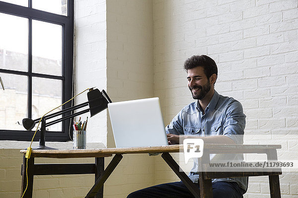 Smiling man woking at desk with laptop