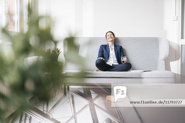 Smiling businesswoman sitting on couch with beverage