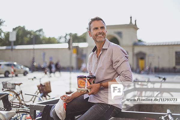 Lächelnder Mann mit Fahrrad und Kaffee zum Mitnehmen in der Stadt