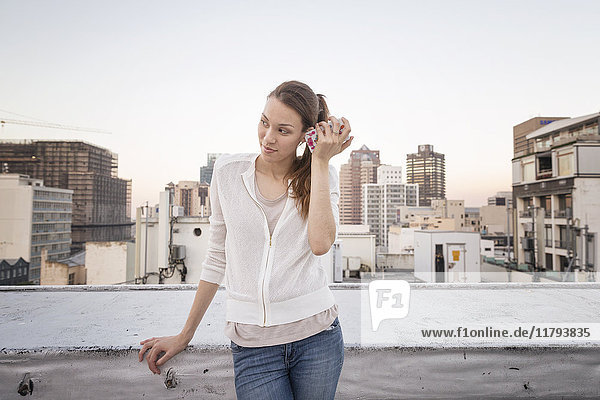 Junge Frau auf einer Dachterrasse stehend  mit Smartphone