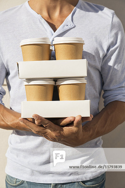 Young man carrying stacks of take away coffee