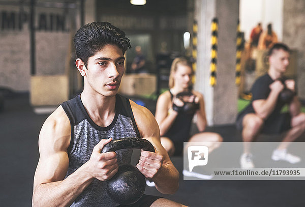 Young man with training partners lifting kettlebell in gym