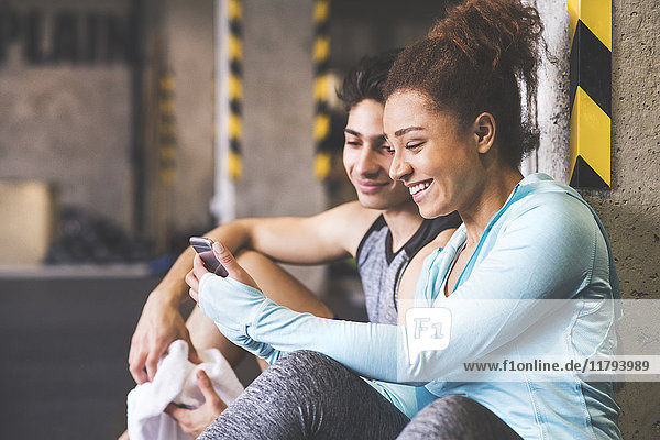 Zwei lächelnde Athleten teilen sich ihr Handy im Fitnessstudio.