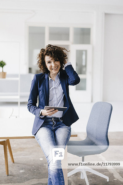 Businesswoman in office sitting on desk  using digital tablet