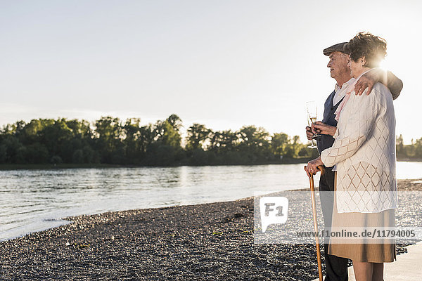 Seniorenpaar am Strand mit Champagnergläsern bei Sonnenuntergang