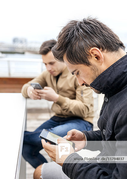 Zwei Männer,  die mit ihren Smartphones Nachrichten senden.