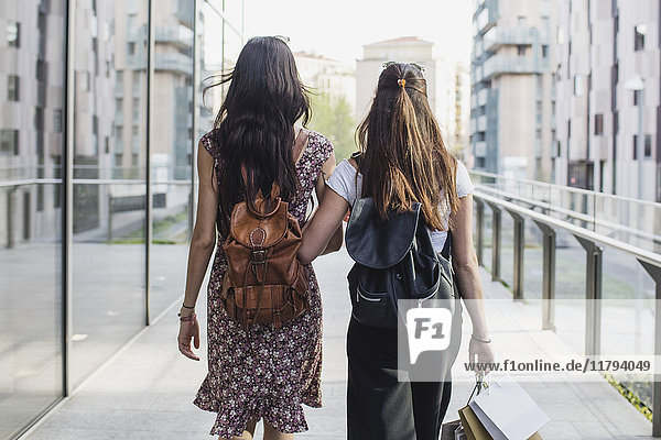 Zwei junge Frauen mit Rucksäcken und Einkaufstaschen laufen durch die Stadt.